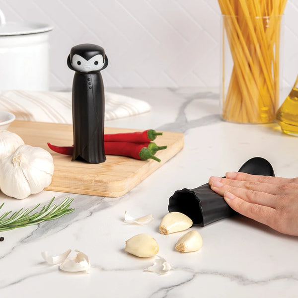 Person using a garlic peeler near ingredients, with a black Drac N Roll kitchen tool standing upright.