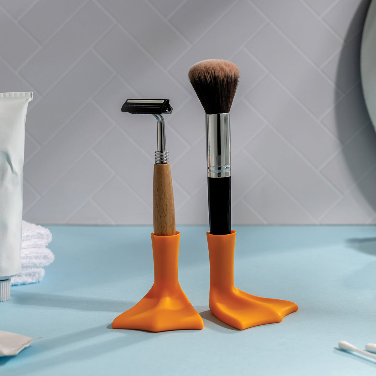 A razor and a Duck-Clean sit upright in orange holders on a blue surface.