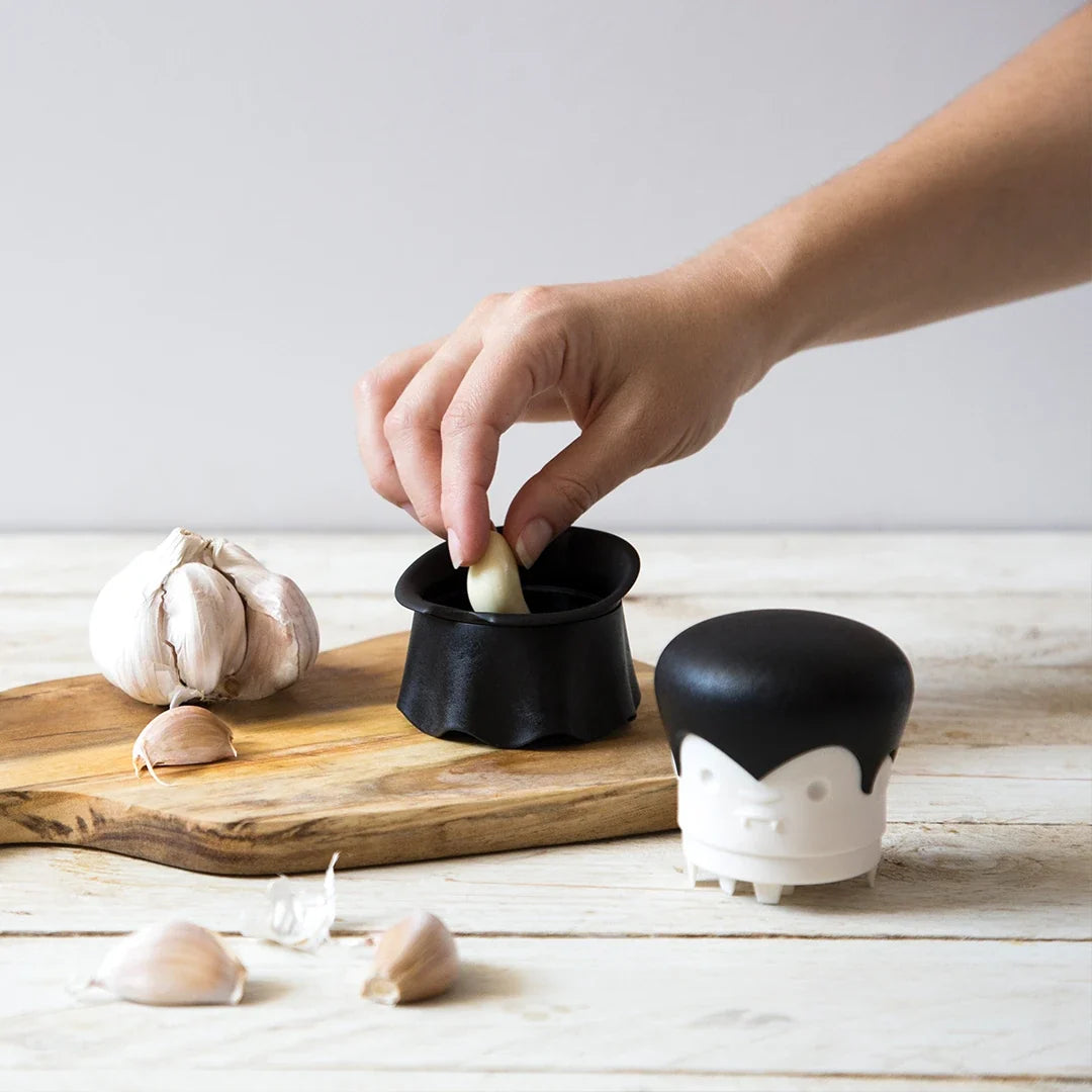 Hand using the Gracula on a wooden board with garlic bulbs.